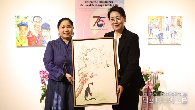 명지대학교 K-민화학과 이미형 주임교수가 주한 필리핀 마리아 테레사 비, 디존-데 베가 대사 에게 민화작품을 기증하고 있다.(사진-담화미디어그룹)