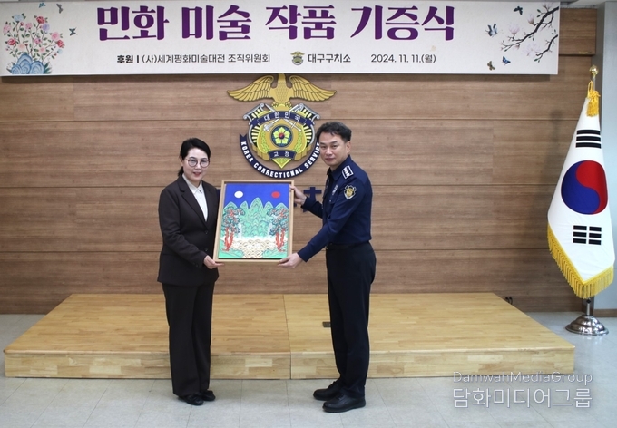 사단법인 세계평화미술대전 조직위원회 민화분과 위원장 이미형(명지대 교수)가 대구 구치소 김영광 소장에게 작품을 전달하고 있다.